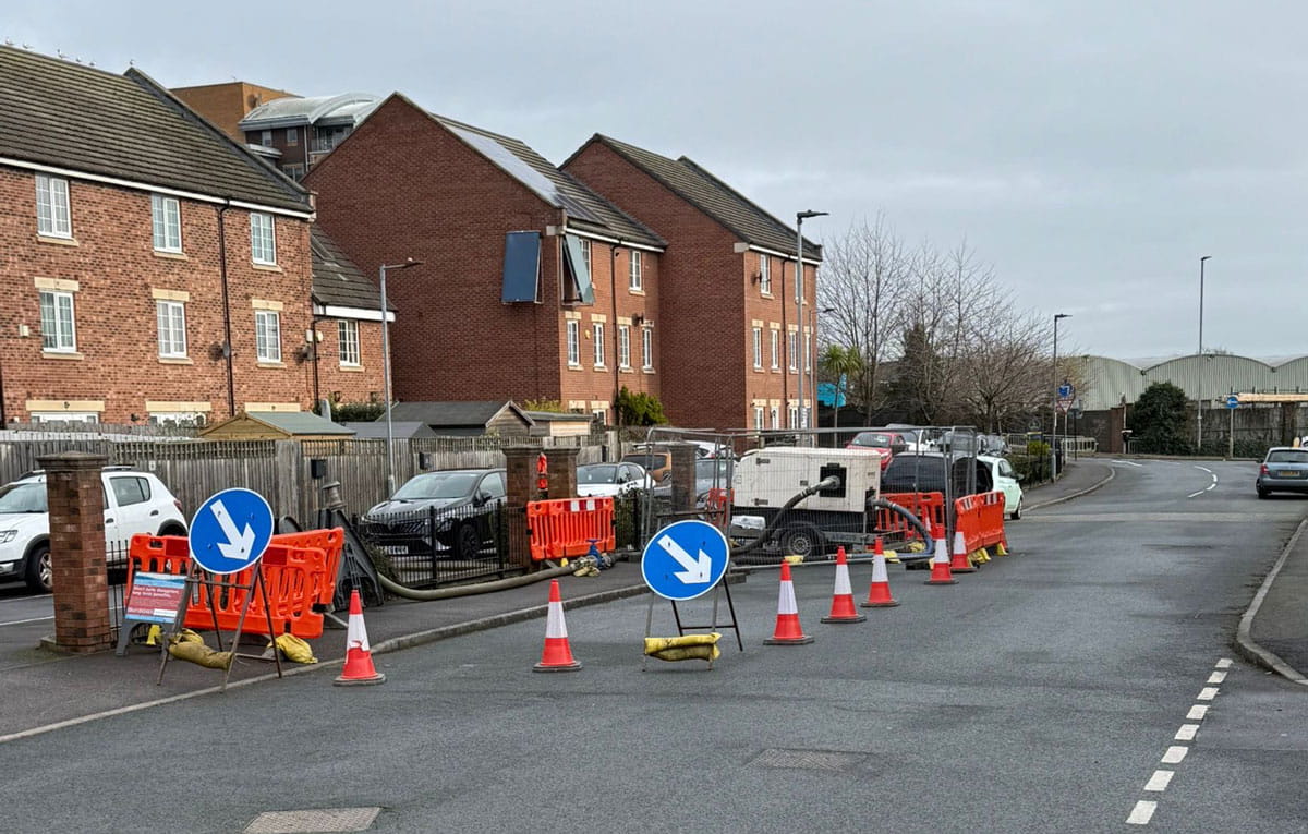 Temporary over-pumping system with generator and hoses installed on a residential street during utility maintenance works.